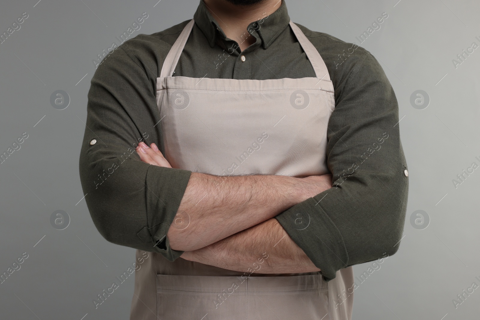 Photo of Man in kitchen apron with crossed arms on grey background. Mockup for design