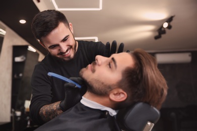 Photo of Professional hairdresser shaving client with straight razor in barbershop