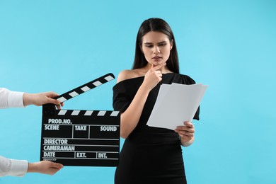 Photo of Actress performing role while second assistant camera holding clapperboard on light blue background. Film industry
