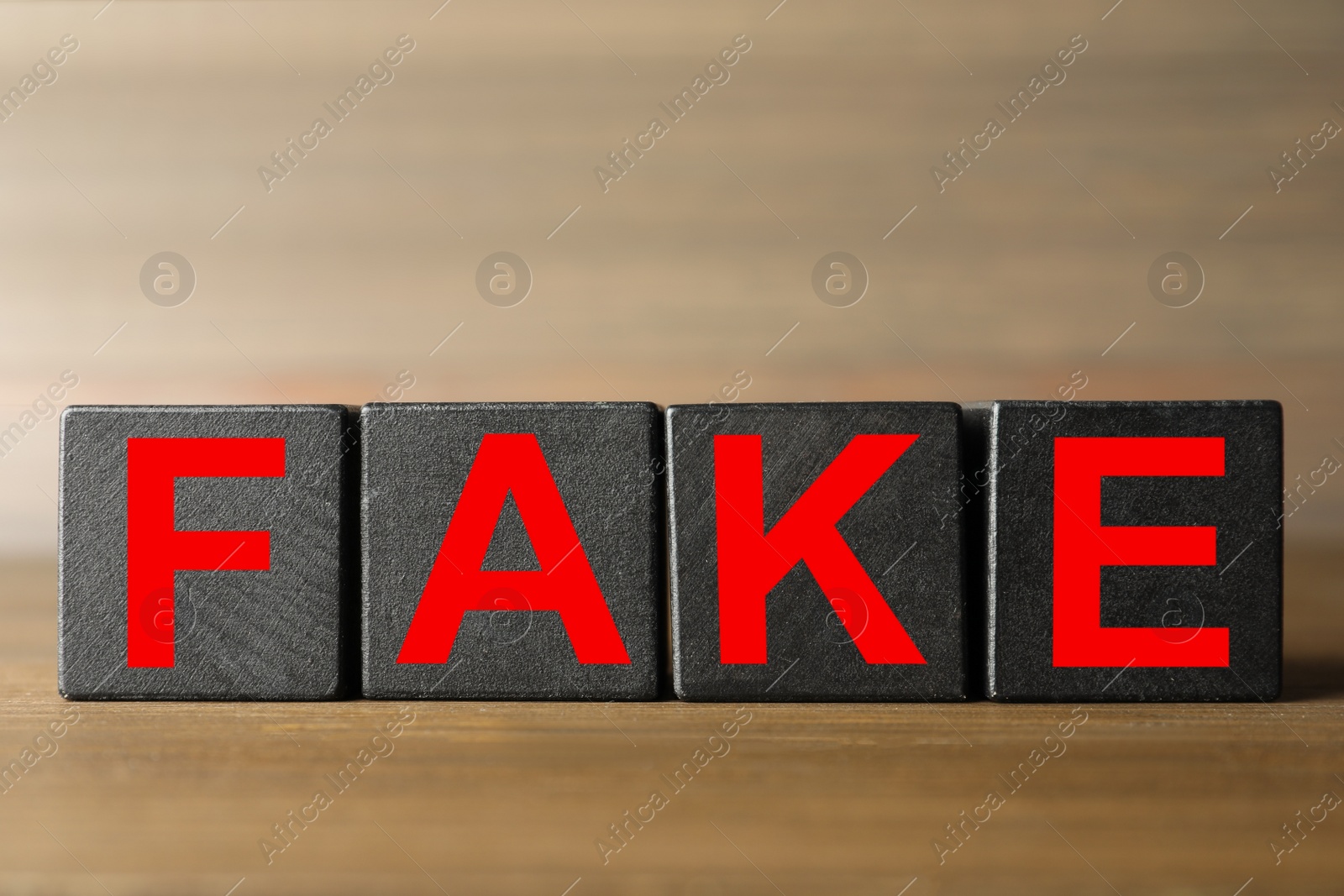 Photo of Word FAKE made with black cubes on wooden table, closeup