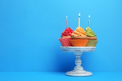 Photo of Birthday cupcakes with candles on stand against color background