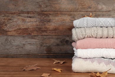 Photo of Stack of warm clothes and autumn leaves on wooden table. Space for text