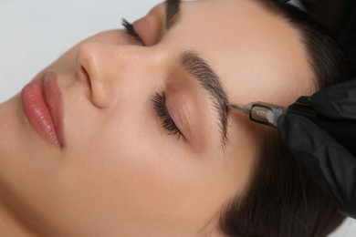 Photo of Beautician making permanent eyebrow makeup to young woman, closeup