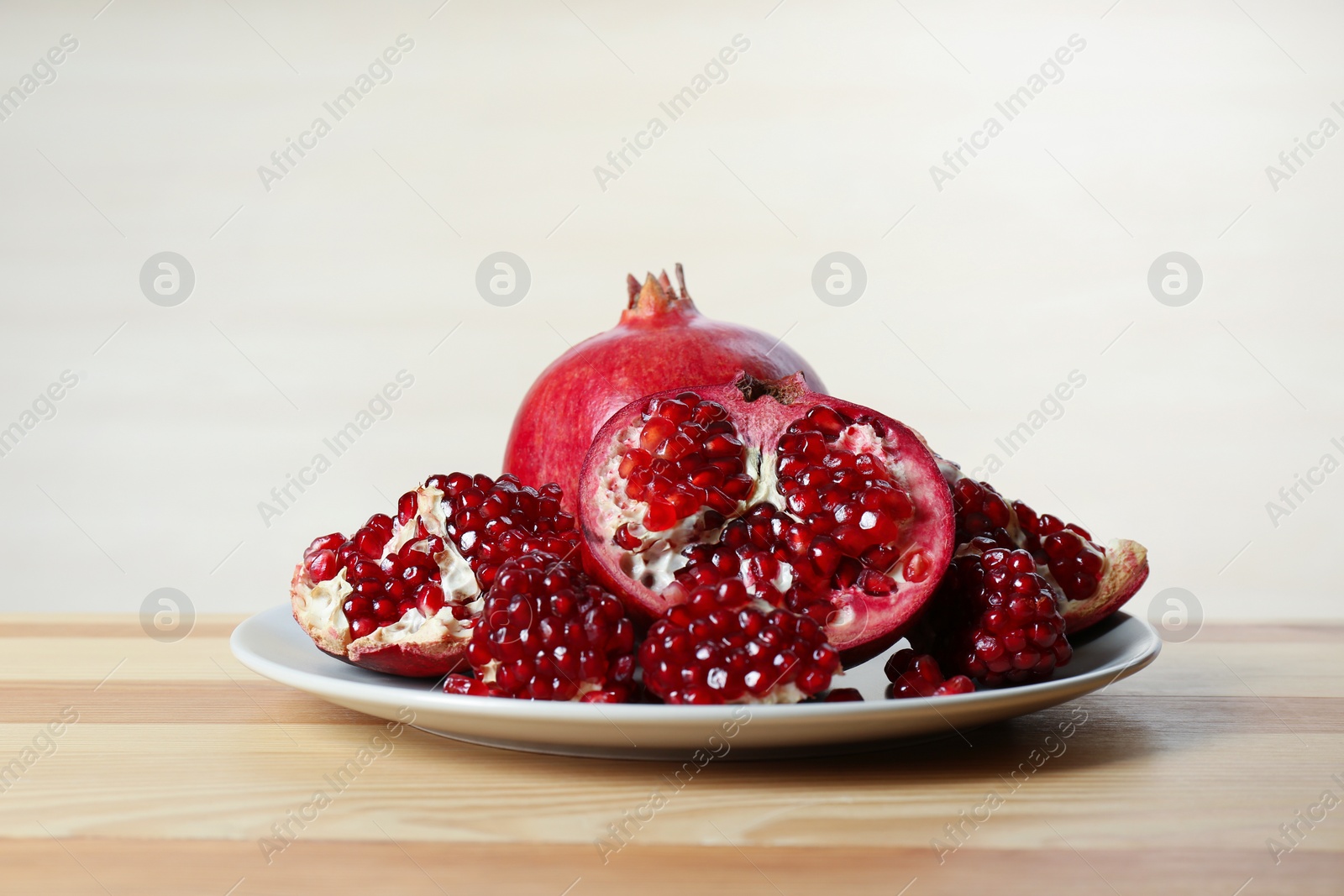 Photo of Plate with ripe pomegranates on table against light background