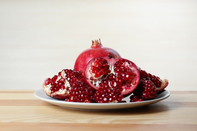 Plate with ripe pomegranates on table against light background