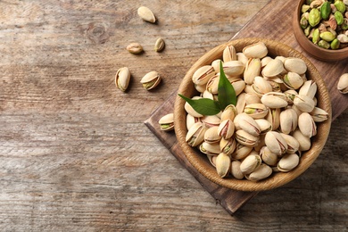 Photo of Organic pistachio nuts in bowl on wooden table, flat lay. Space for text