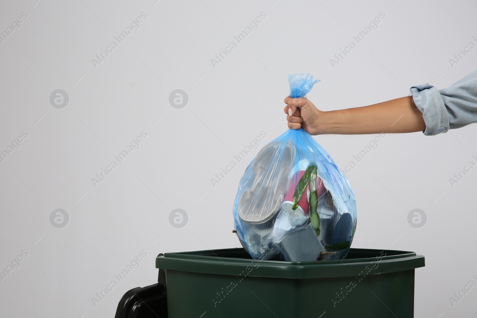 Photo of Woman throwing garbage bag into bin on light background, closeup. Space for text