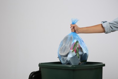 Woman throwing garbage bag into bin on light background, closeup. Space for text