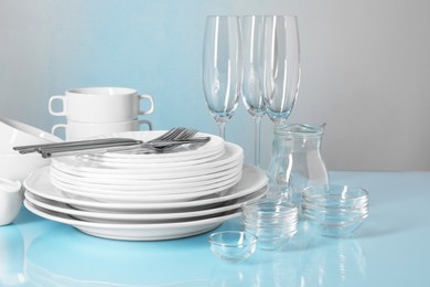 Photo of Set of clean dishes, glasses and cutlery on light blue table