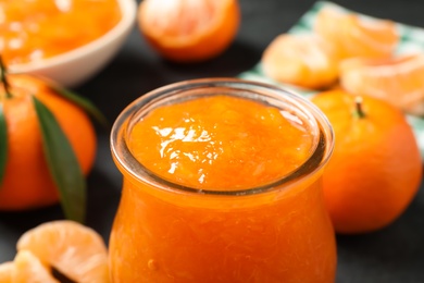 Photo of Tasty tangerine jam in glass jar on dark table, closeup