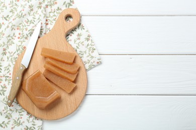 Photo of Tasty sweet quince paste and knife on white wooden table, top view. Space for text