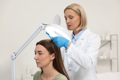 Trichologist examining patient`s hair under lamp in clinic