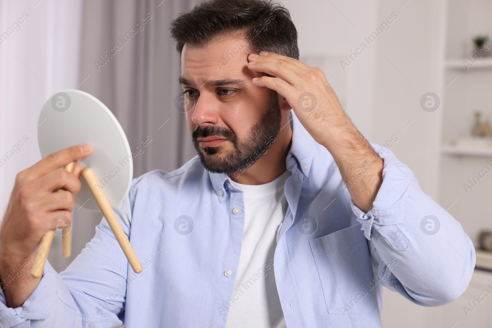 Photo of Confused man with skin problem looking in mirror at home