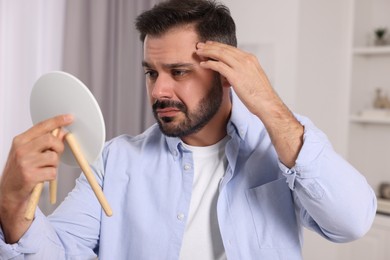 Photo of Confused man with skin problem looking in mirror at home