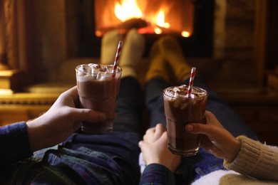 Photo of Couple with glasses of hot cocoa near fireplace at home, closeup