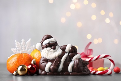 Photo of Composition with chocolate Santa Claus, sweets, tangerine and Christmas decorations on light background