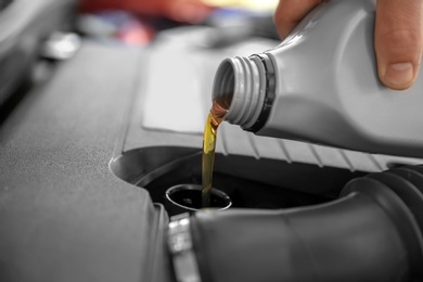 Mechanic pouring oil into car engine, closeup