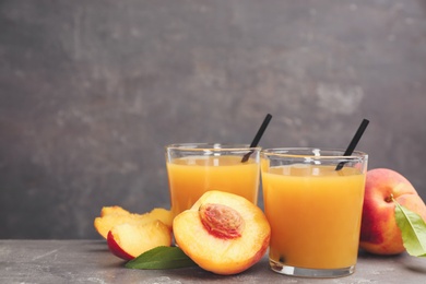Photo of Natural peach juice and fresh fruits on grey table. Space for text