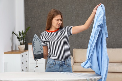 Emotional woman with iron and shirt at home