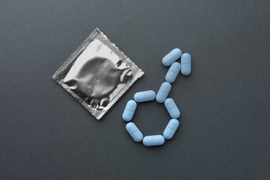 Male sign made of pills and condom on dark gray background, flat lay. Potency problem