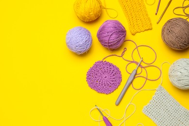 Flat lay composition with knitting threads and crochet hooks on yellow background, space for text