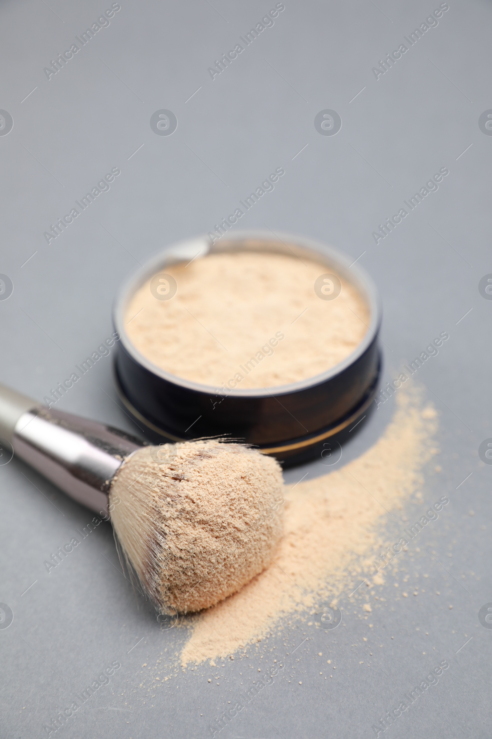 Photo of Loose face powder and makeup brush on light grey background, closeup