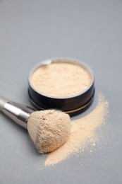 Photo of Loose face powder and makeup brush on light grey background, closeup