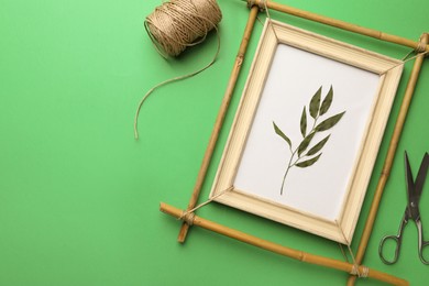 Photo of Bamboo frame with dried plant, scissors and twine on green background, flat lay. Space for text