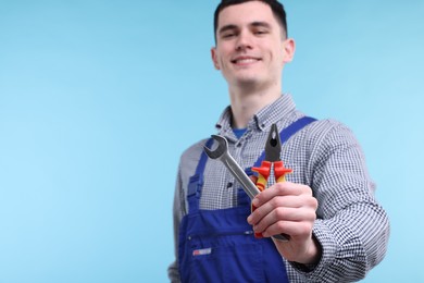 Young man holding pliers on light blue background, selective focus. Space for text