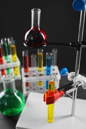 Photo of Retort stand and laboratory glassware with liquids on table against black background, closeup