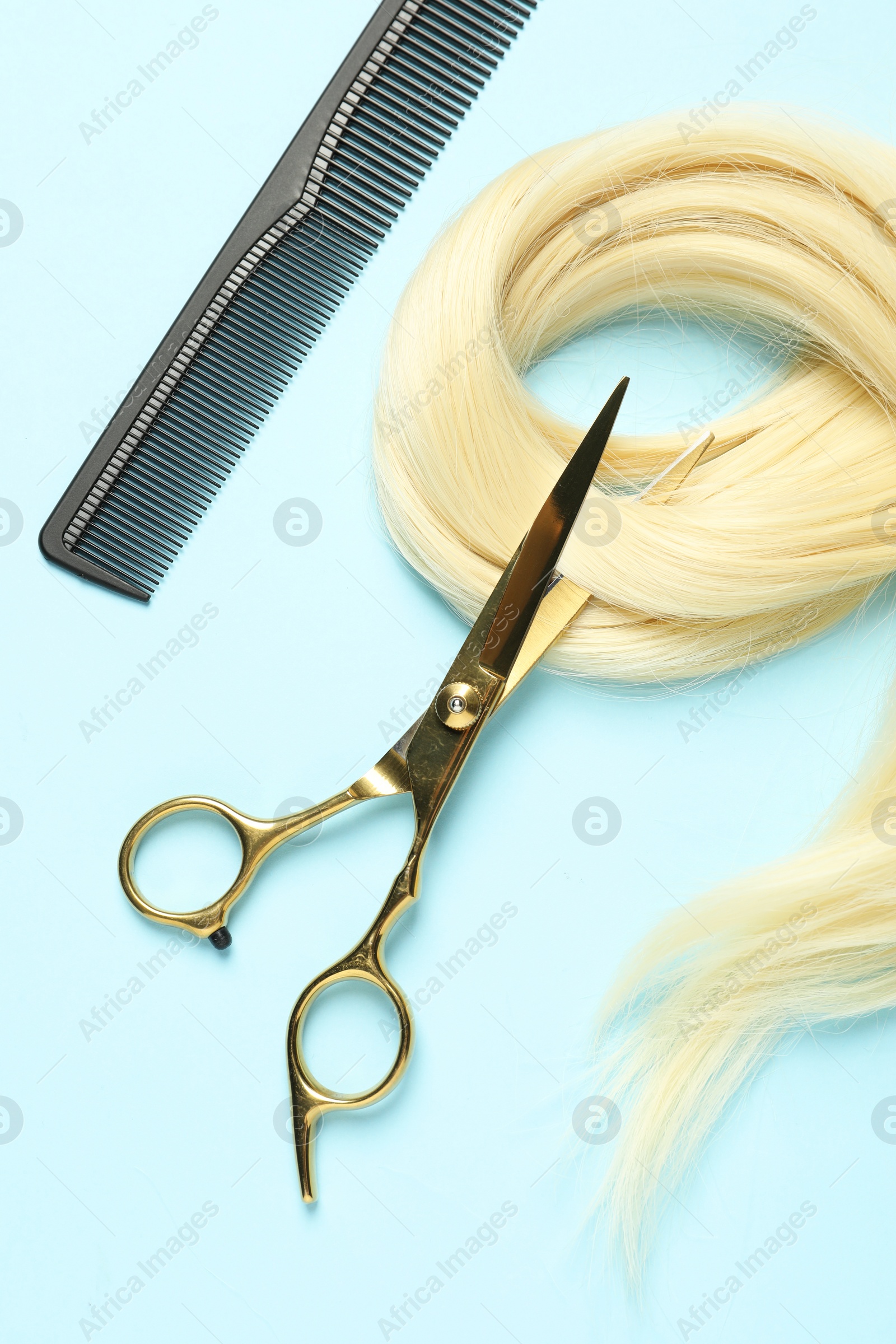 Photo of Professional hairdresser scissors and comb with blonde hair strand on light blue background, flat lay