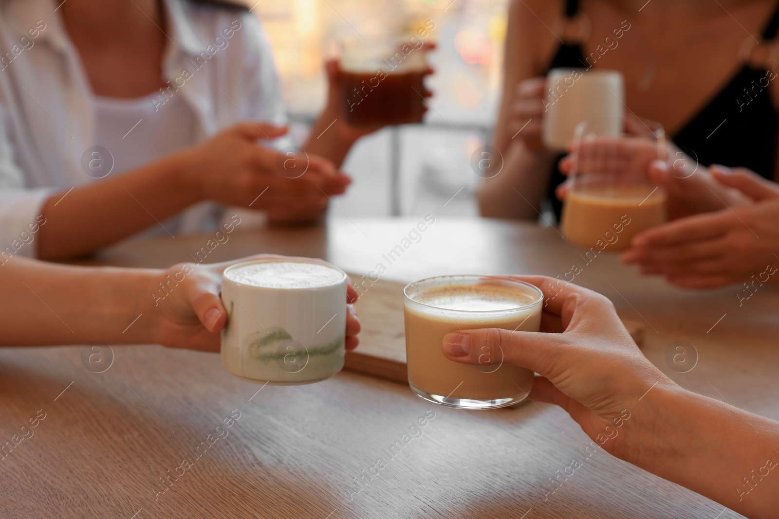 Photo of Friends drinking coffee at wooden table in cafe, closeup