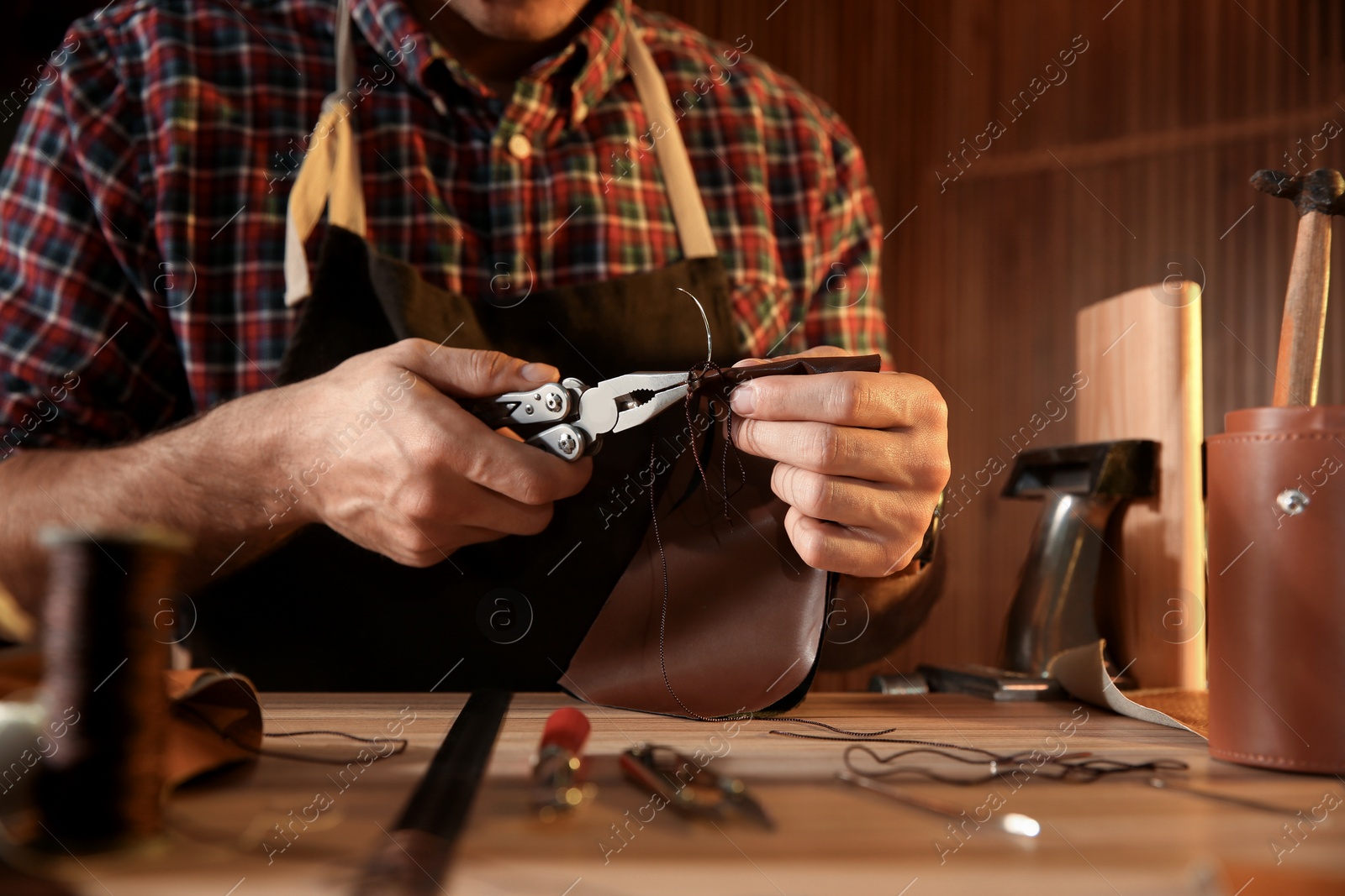 Photo of Man sewing piece of leather at table, closeup