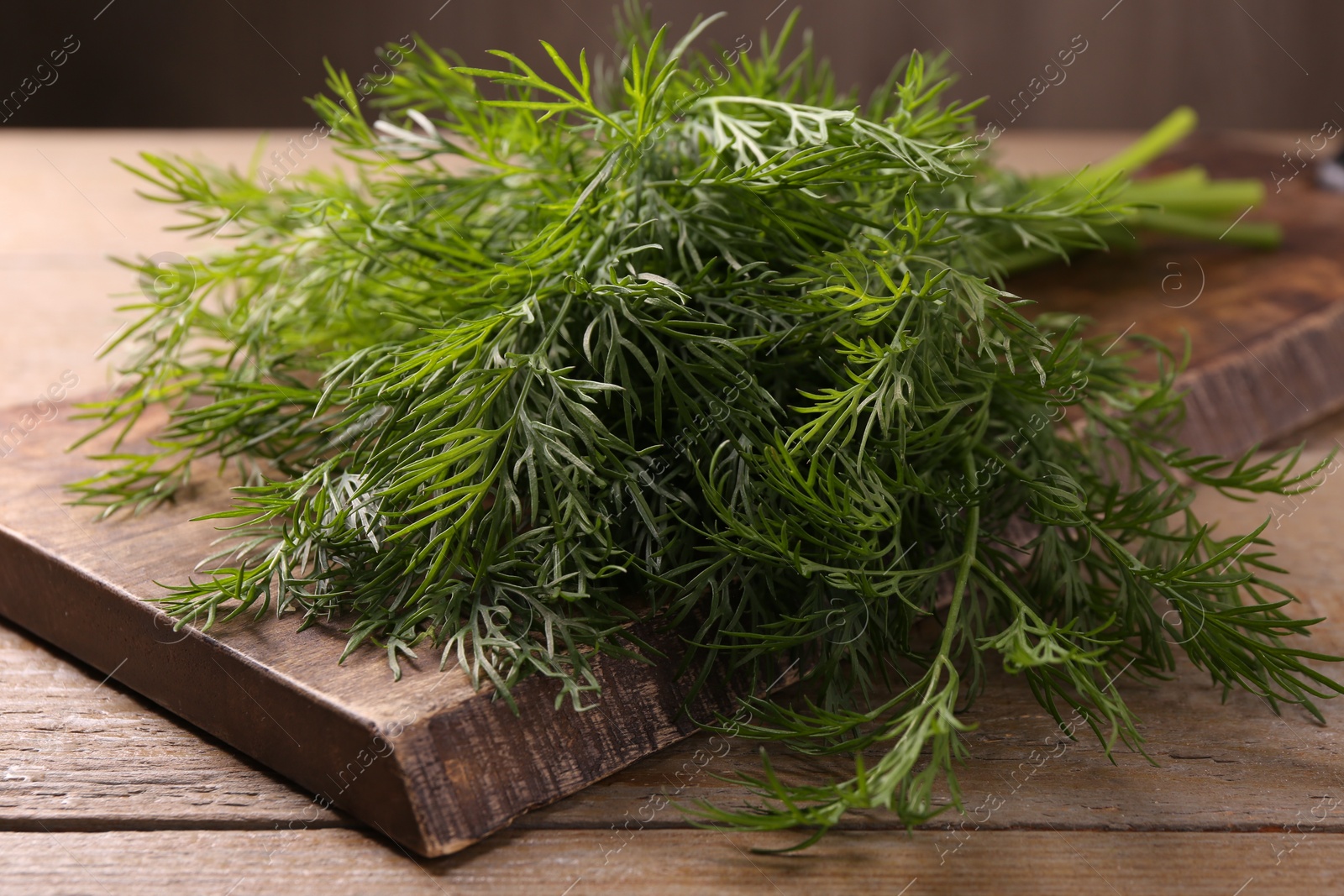 Photo of Board with sprigs of fresh dill on wooden table, closeup