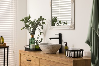 Photo of Modern bathroom interior with stylish mirror, eucalyptus branches, vessel sink and wooden vanity