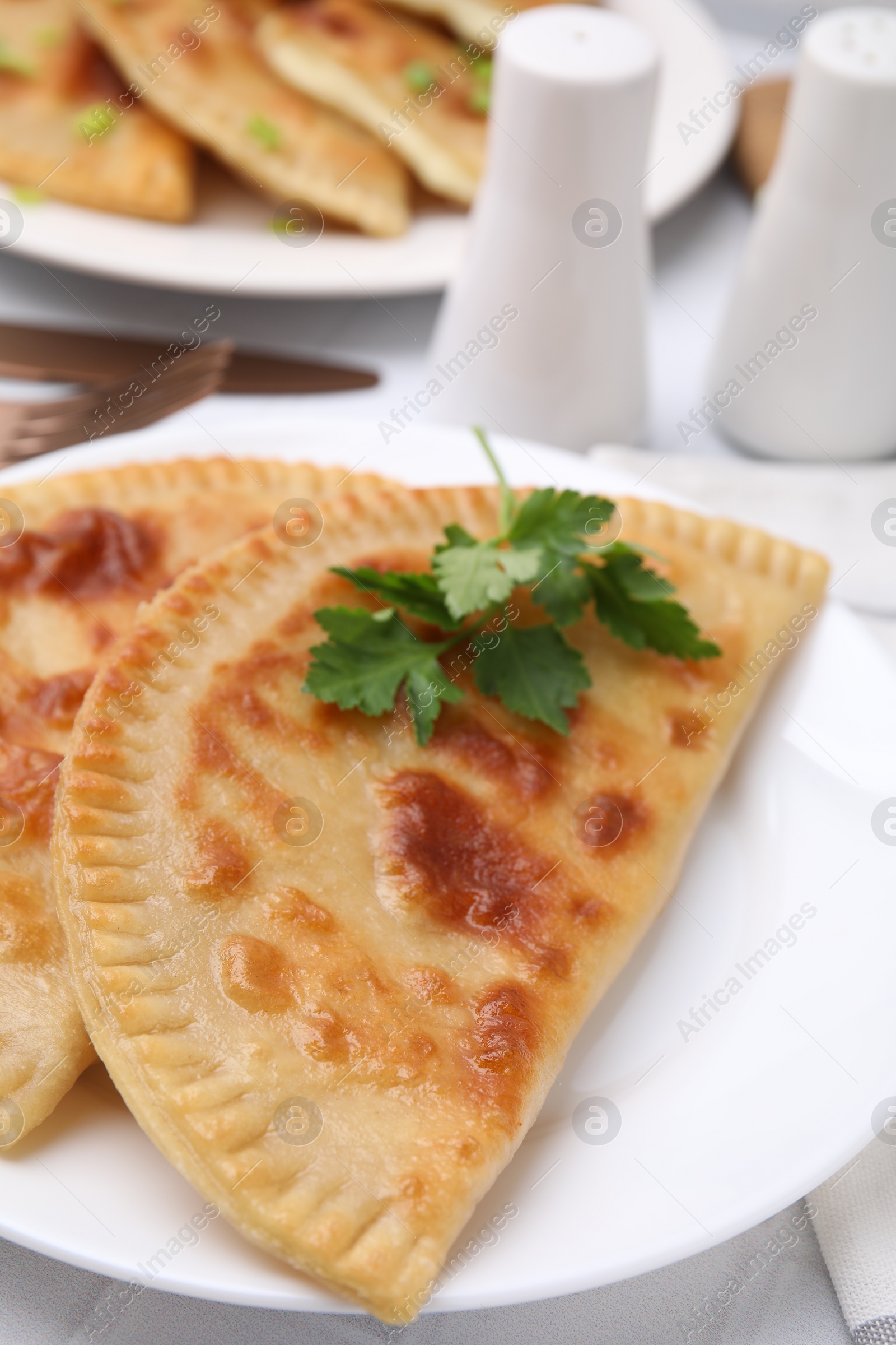 Photo of Delicious fried cheburek with cheese and parsley on white tiled table, closeup