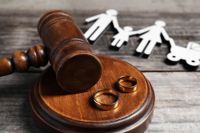 Divorce concept. Gavel, wedding rings and paper cutout of family on wooden table, closeup