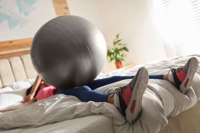 Photo of Lazy young woman with exercise ball sleeping on bed, focus on legs