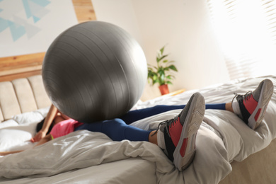 Lazy young woman with exercise ball sleeping on bed, focus on legs