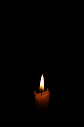 Photo of Bright burning wax candle on black background
