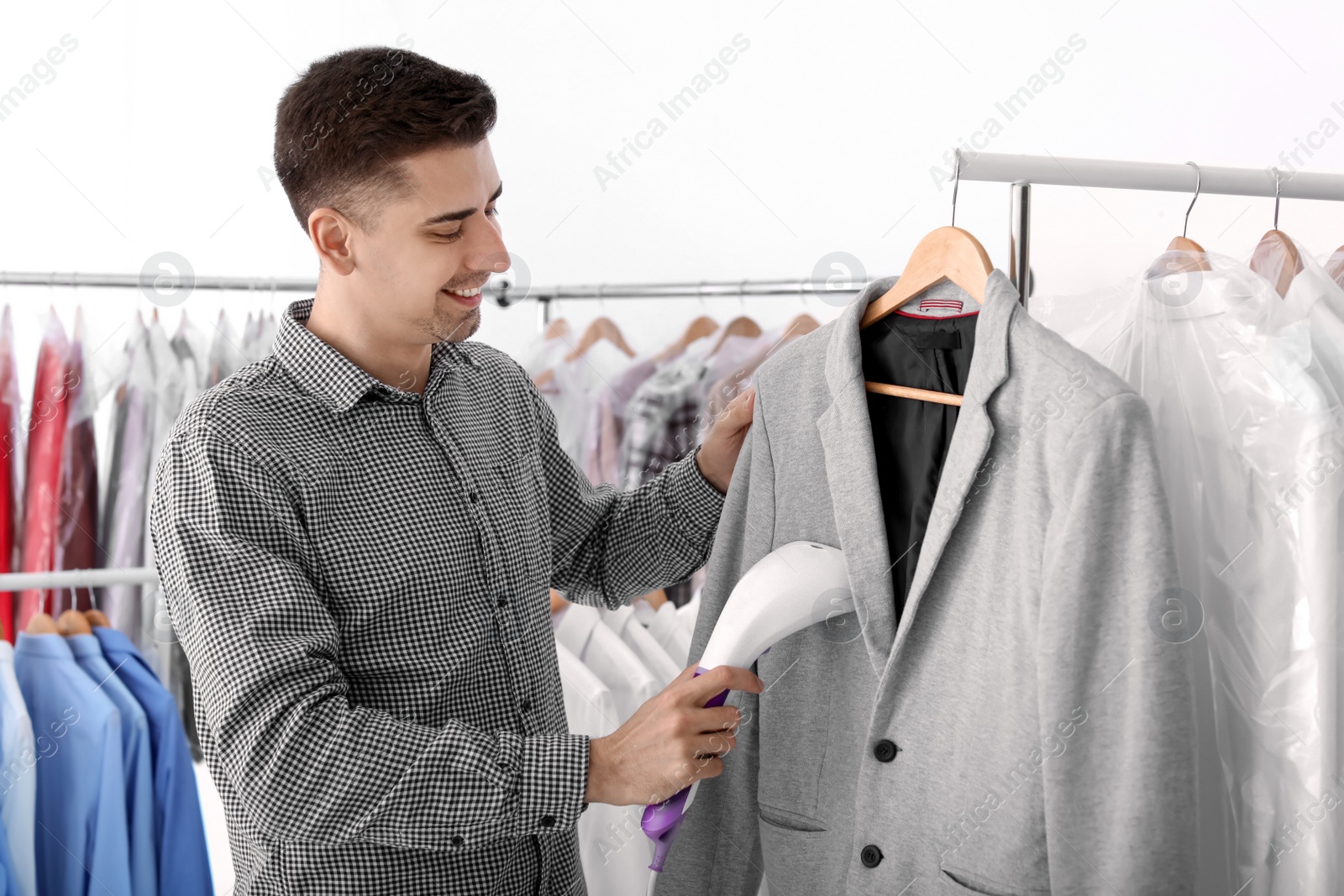 Photo of Young man steaming jacket at dry-cleaner's