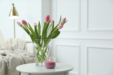 Photo of Beautiful tulips and burning candle on white table indoors, space for text. Interior design