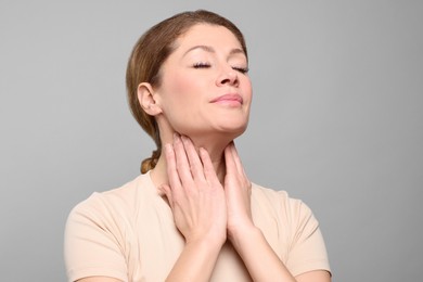 Woman suffering from sore throat on light grey background