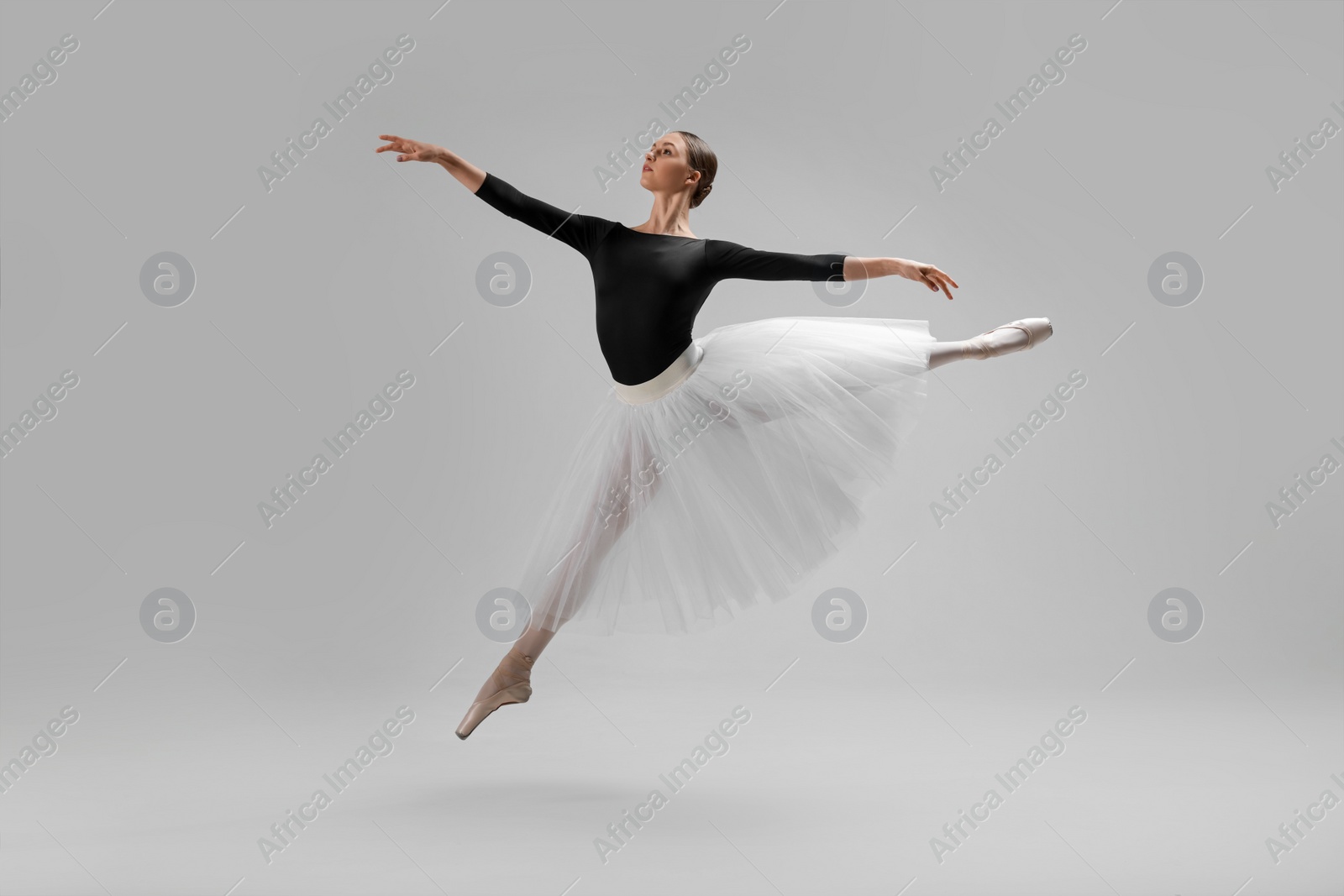 Photo of Young ballerina practicing dance moves on light grey background