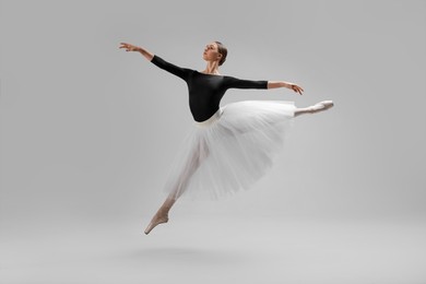 Young ballerina practicing dance moves on light grey background
