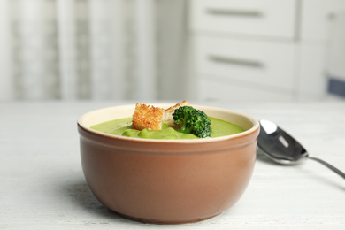 Photo of Delicious broccoli cream soup with croutons served on white wooden table indoors