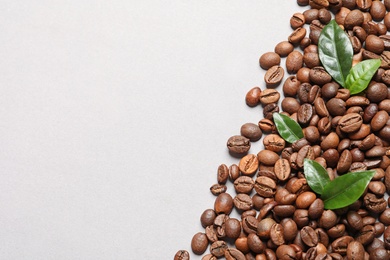 Fresh green coffee leaves and beans on light background, flat lay. Space for text