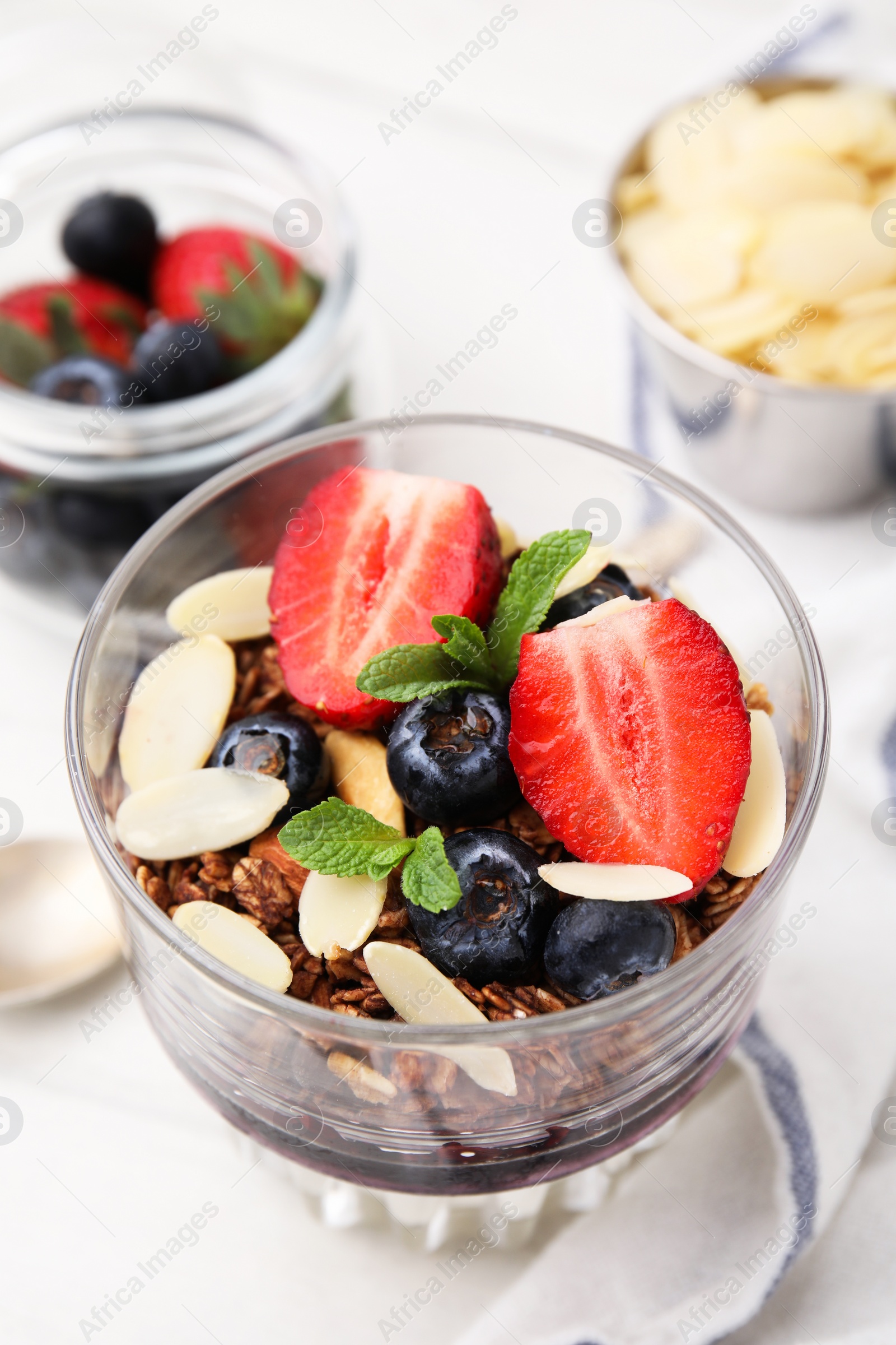 Photo of Tasty granola with berries, jam and almond flakes in glass on white table, closeup