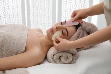 Photo of Young woman receiving facial massage with gua sha tools in beauty salon