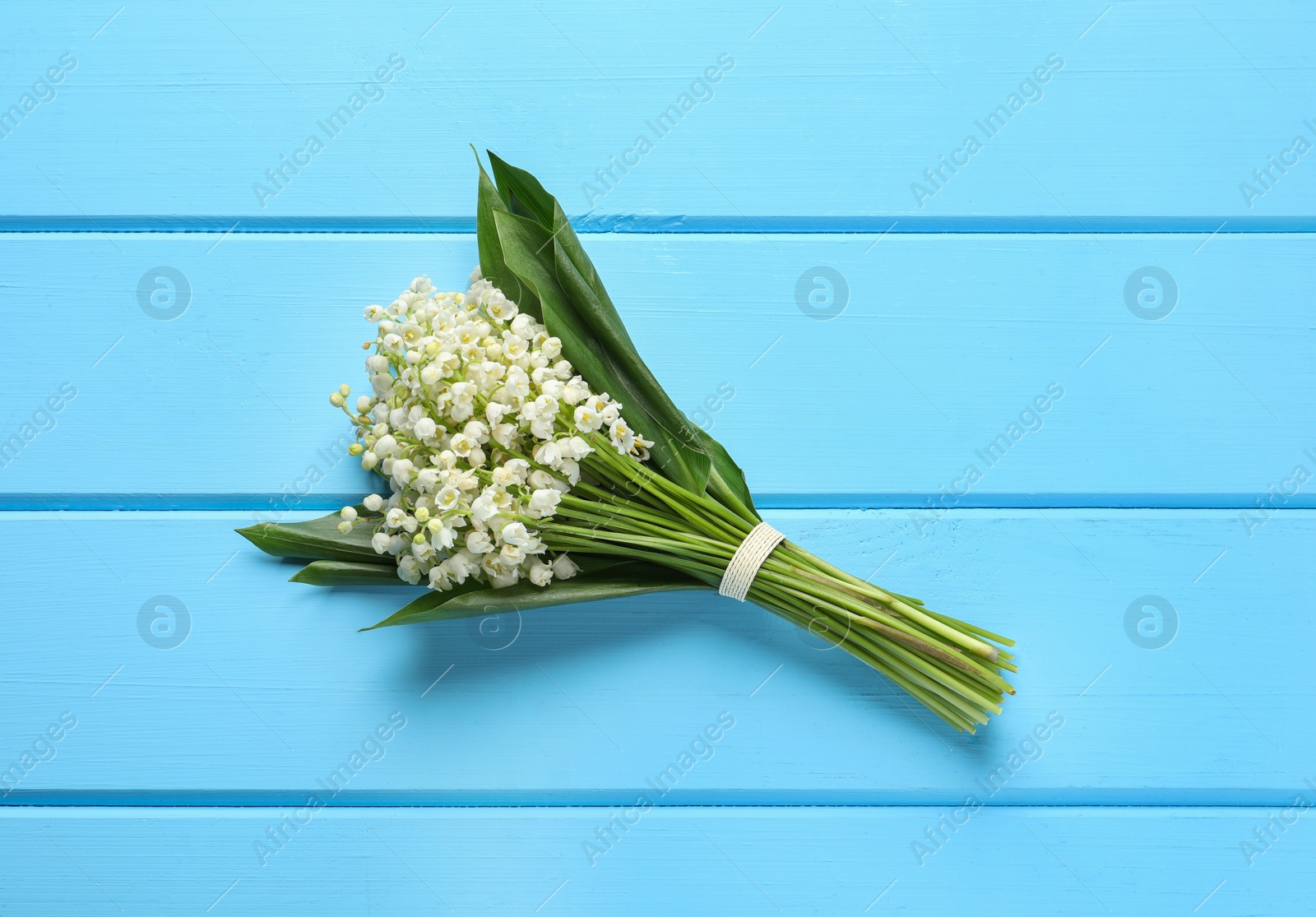 Photo of Beautiful lily of the valley bouquet on light blue wooden table, top view